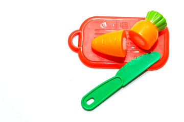 childrens plastic toy. plastic carrot on red cutting board with green knife isolated on white background in soft-focus in the background