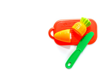 childrens plastic toy. plastic carrot on red cutting board with green knife isolated on white background in soft-focus in the background