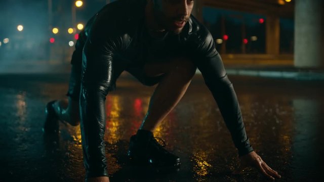Strong Muscular Fit Young Man Starts Sprinting on a Rainy Evening. He is Running in an Urban Environment Under a Bridge with Cars in the Background.