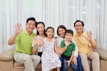 Happy big Asian family sitting on sofa and waving at camera