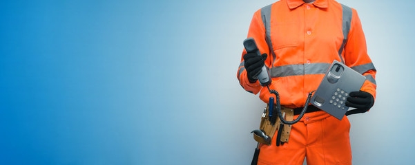 Builder worker is holding in hand a handset phone isolated on blue background with copy space. Call...