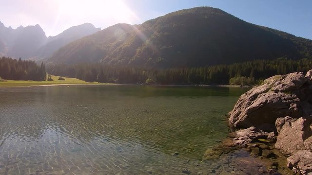 Pan reveal to the right side of a glacial like in the mountains. Pasture, grass, forest and mountains are visible on a bright warm sunny summer day.
