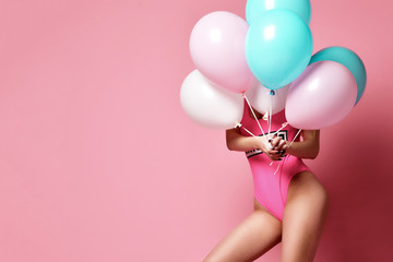 Woman on birthday party having fun hide behind pastel color air balloons on pink 