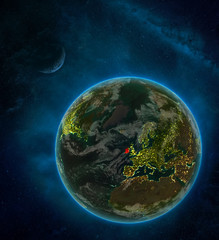 Ireland from space on Earth at night surrounded by space with Moon and Milky Way. Detailed planet with city lights and clouds.