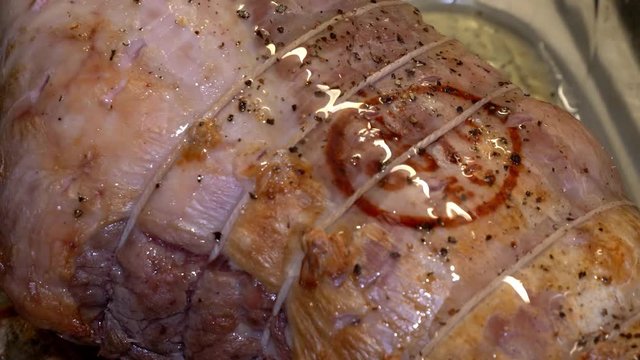 Slow motion close up of pouring oil on top of a halfway cooked a joint of pork in a glass oven dish