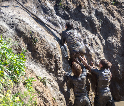 Young people pass the obstacle course. Mud race runners. Climbing the rope. Teamwork.