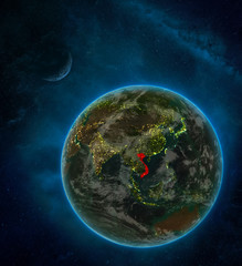 Vietnam from space on Earth at night surrounded by space with Moon and Milky Way. Detailed planet with city lights and clouds.