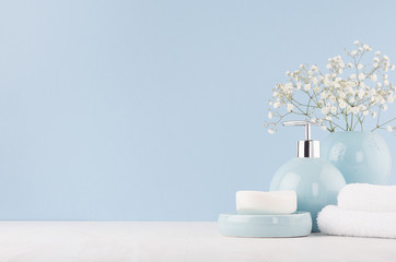 Soft light fresh bathroom interior in pastel blue color with white bouquet, smooth ceramic bowls, cosmetic products on wood table.