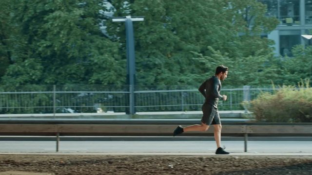 Athletic Young Man in Sports Outfit is Jogging in the Street. He is Running in an Urban Environment Under a Brindge with Cars in the Background.