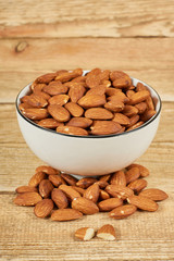 Peeled almond nuts in the white bowl on wooden table with copy space, close-up