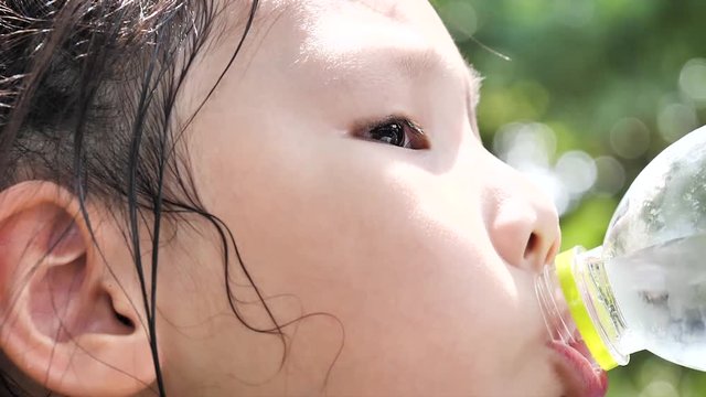 Child drinking water from bottle outdoor. Young girl with water bottle in hand at park, slow motion.