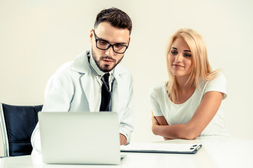 Male doctor talks to female patient in hospital office while looking at the patients health data on...