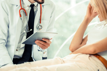 Male doctor is talking and examining female patient in hospital office. Healthcare and medical...