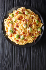 Pasta with Brussels sprouts, ham covered with creamy cheese sauce close-up on a plate. Vertical top view