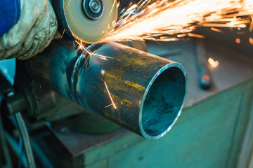 mechanic cleans a welded seam on a section of a steel pipe with the help of a grinding machine in the metal workshop