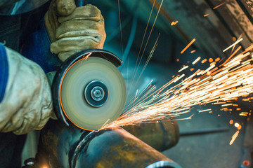worker cut a welded seam on a section of a steel pipe with the help of a grinding machine in the...
