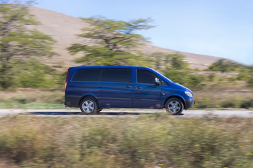 Minibus drives along the road against hilly background.