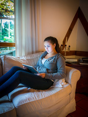 Young girl in casual clothes is reading on a tablet computer at home, Hessen, Germany