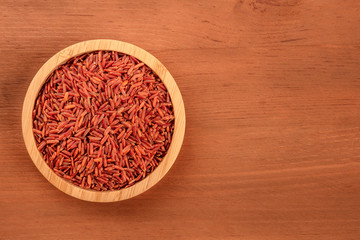 Red rice, shot from the top in a wooden bowl on a dark rustic background with a place for text