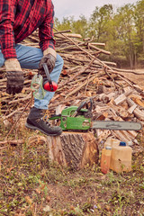 Lumberjack with chainsaw and pile of cut woods.