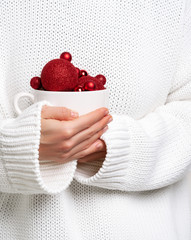 Woman in warm white sweater holding mug with christmas balls like ice cream. Concept for New year mockup.