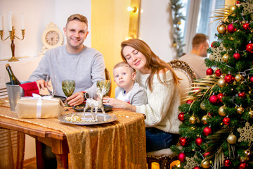 Happy young family, father, mother and son, in Christmas evening in home. They sitting at the table at Christmas dinner. New Year's and Christmas theme. Holiday mood
