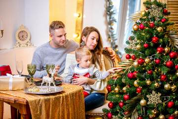 Happy young family, father, mother and son, in Christmas evening in home. They sitting at the table at Christmas dinner. New Year's and Christmas theme. Holiday mood