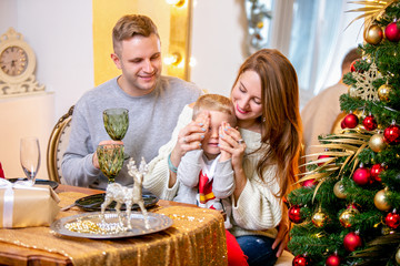 Happy young family, father, mother and son, in Christmas evening in home. They sitting at the table at Christmas dinner. New Year's and Christmas theme. Holiday mood