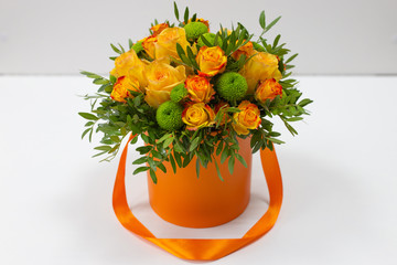 Bright bouquet of orange roses and green flowers in an orange box for hats on a light background