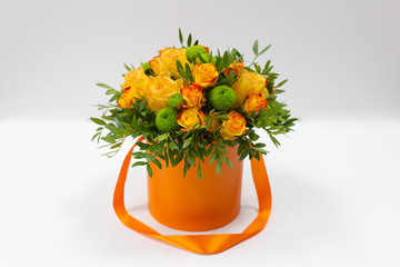 Bright bouquet of orange roses and green flowers in an orange box for hats on a light background