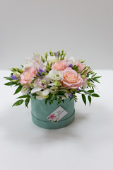 Delicate bouquet of white and pink roses and orchids with green leaves in a hat box of cerulean color on a light background