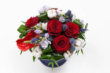 A bright bouquet of red flowers (rose and anthurium) with green leaves, Alstroemeria and cotton flowers in a blue box for hats on a light background