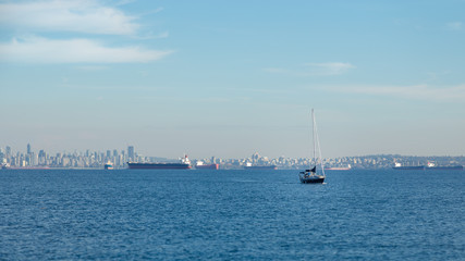 Fototapeta premium Vancouver skyline with a sailboat and tanker ships on a sunny day.