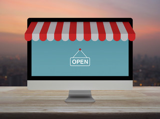 Desktop modern computer monitor with online shopping store graphic and open sign on wooden table...
