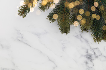 Christmas fir tree branches and bokeh blurred fairy lights on a marble background