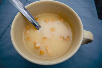 Chicken cream soup with croutons in a yellow cup on a gray background.