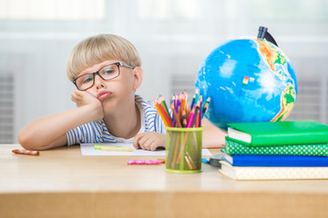 Cute child boring on the lesson. Kid doesn`t want to do homework or classwork. Unhappy schoolboy.