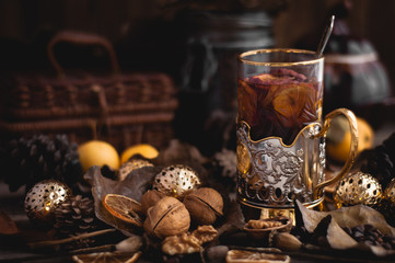 Tea with apples in a Cup holder on the background of nuts, leaves, dried flowers on a wooden table. Brown tone.
