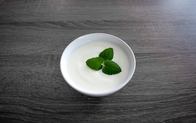 Ceramic bowl with white plain yogurt and mint leaves isolated on dark wooden background from above