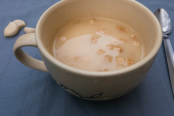 Chicken cream soup with croutons in a yellow cup on a gray background.