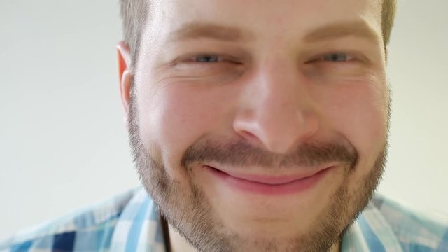 Young stylish blue-eyed male with a beard looks into the camera and quickly blinks his eyes, love, closeup, white background, caucasian