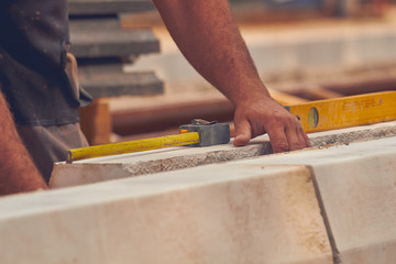 Real construction worker with measuring tape leveling concrete blocks.