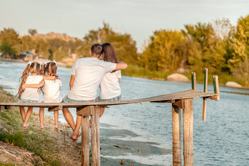 summertime, portrait of an happy family sitting on the edge of a wooden pontoon, feet in the river