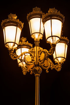 Night view of five beautiful decorative bronze street lights together on a lampost outdoors.