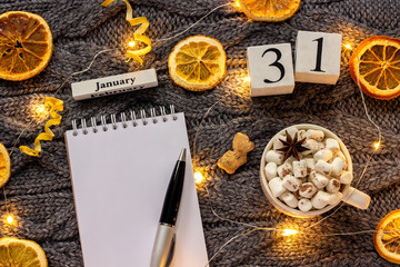 Winter composition. Wooden calendar January 31st Cup of cocoa with marshmallow, empty open notepad with pen, dried oranges, light garland on grey knitted background. Top view Flat lay Mockup - Powered by Adobe