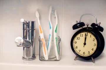 Dental hygiene time concept. Black alarm clock in the washroom next to toothbrushes.