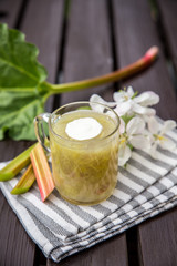 Sweet and sour kissel or kisel dessert made of an rhubarb (Rheum rhabarbarum) with the spash of whipped cream in a clear cup on a wooden background. Traditional dessert in Estonia, popular in spring.