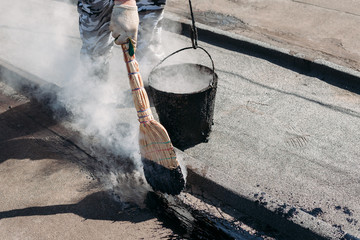 Worker repairs the roof with molten tar from a bucket with a broom. - obrazy, fototapety, plakaty