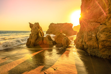 Fototapeta premium El Matador State Beach, Kalifornia, Stany Zjednoczone. Promienie słoneczne ze światłami zachodu słońca między filarami i formacjami skalnymi najczęściej fotografowanych i malowniczych plaży Malibu na Oceanie Spokojnym. Zachodnie wybrzeże Kalifornii