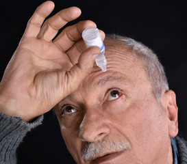 Obraz premium Senior man dripping a red bloodshot eye with eye drops